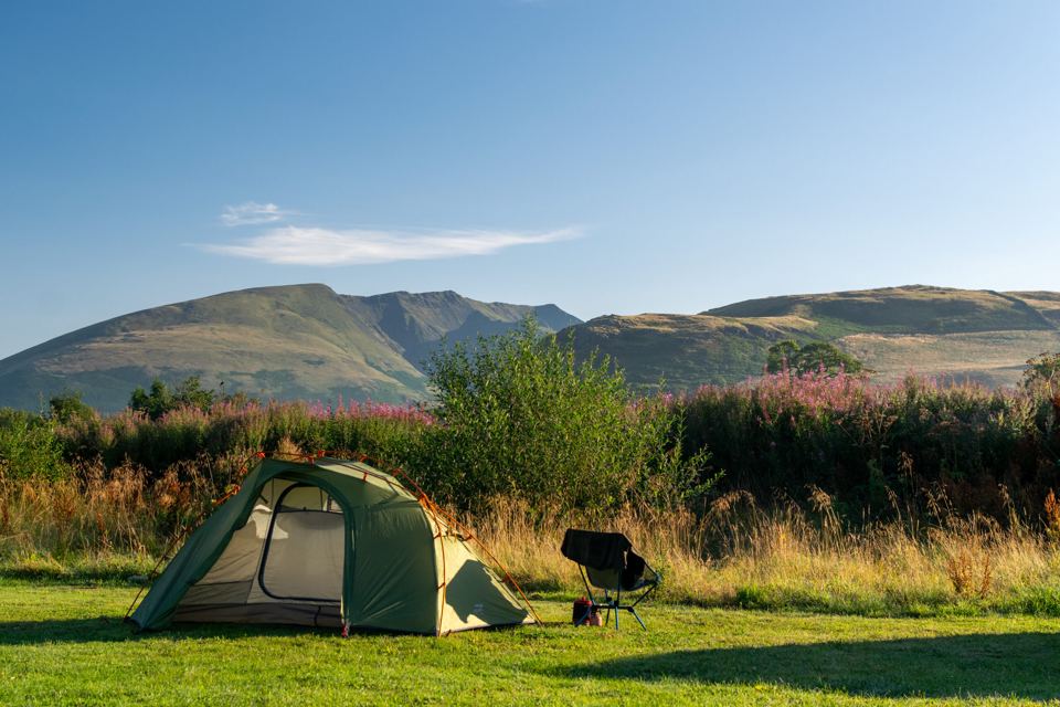Tent pitched in long grass with hills