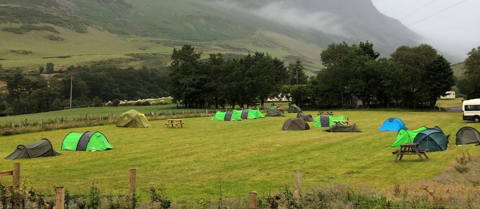 Tents in the grass field below the hills